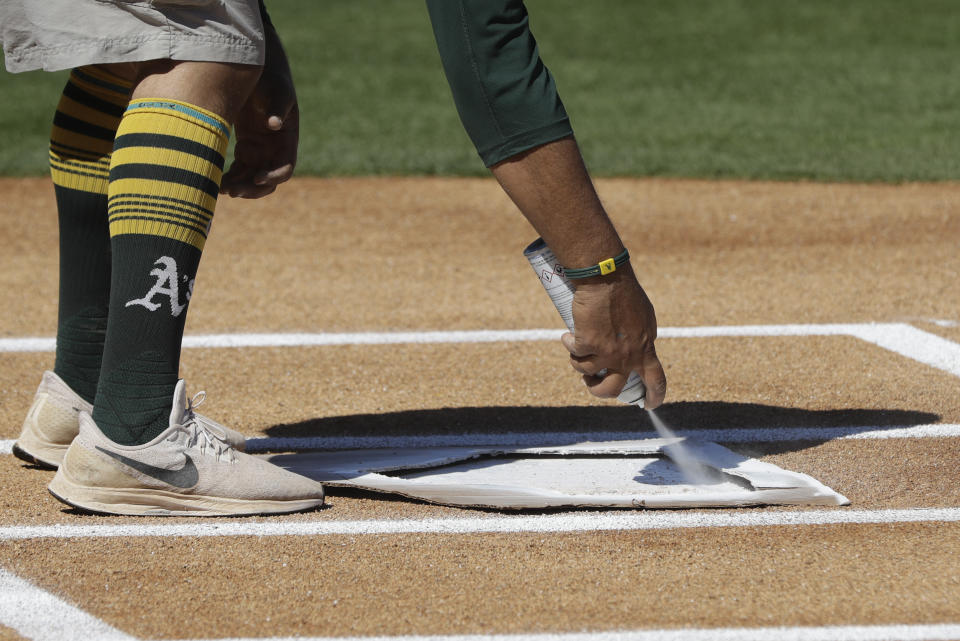 An Oakland Athletics grounds crew member paints home plate before during a spring training baseball game between the Oakland Athletics and the Cleveland Indians, Saturday, Feb. 29, 2020, in Mesa, Ariz. (AP Photo/Darron Cummings)