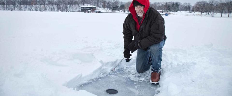 A smiling middle aged man ice fishing on a snowy lake in Minnesota during the winter