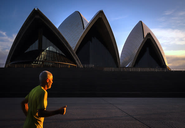 A runner passes the iconic landmark of the Sydney Opera House during sunrise.