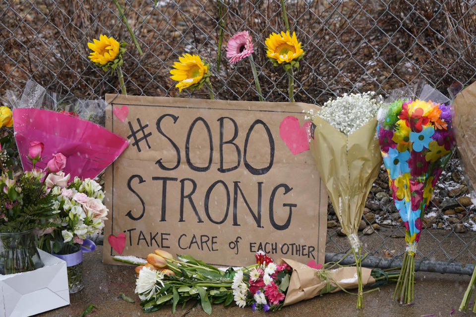 A sign from residents of south Boulder stands amid bouquets left along a fence put up around the parking lot where a mass shooting took place in a King Soopers grocery store Tuesday, March 23, 2021, in Boulder, Colo. (AP Photo/David Zalubowski)