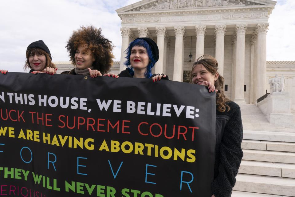 Amelia Bonow, left, with her cousin Lila Bonow, Emily Nokes, and Sara Edwards, all with the group, "Shout Your Abortion," hold a sign outside of the Supreme Court, Tuesday, Nov. 30, 2021, as activists begin to arrive ahead of arguments on abortion at the court on Capitol Hill in Washington. (AP Photo/Jacquelyn Martin)