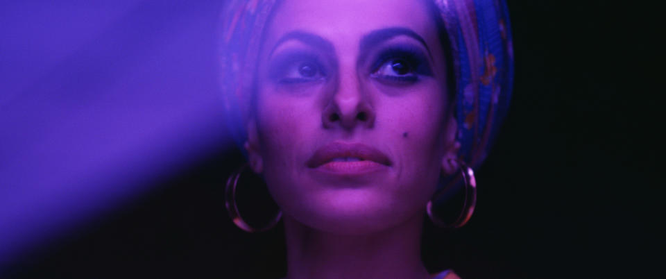 closeup of Eva in hoop earrings and a headscarf looking to the side under dark lighting