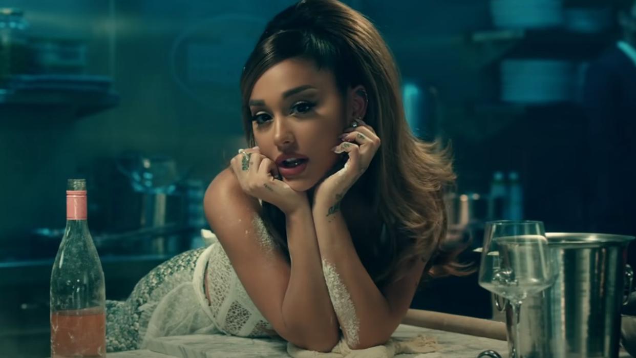  Ariana Grande leaning against her hand standing in a kitchen in the Positions music video. 