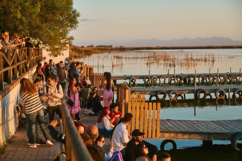 People gathered on a jetty next to a lake watching the sunset