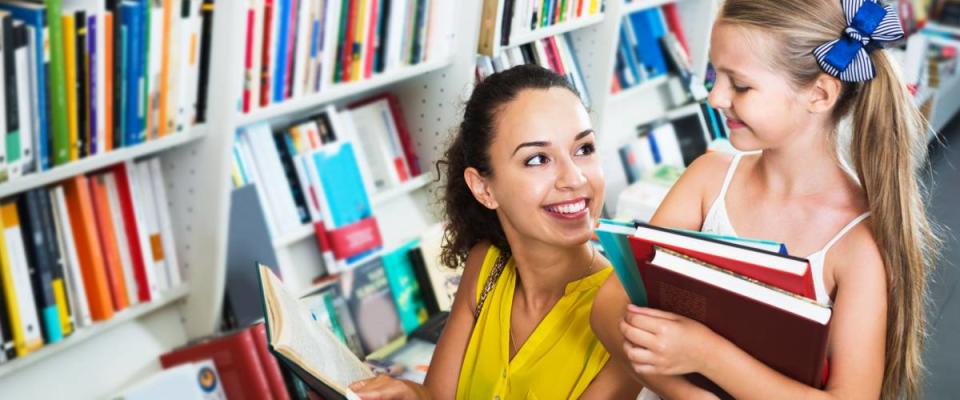 Portrait of smiling young mother with daughter reading textbook in book shop