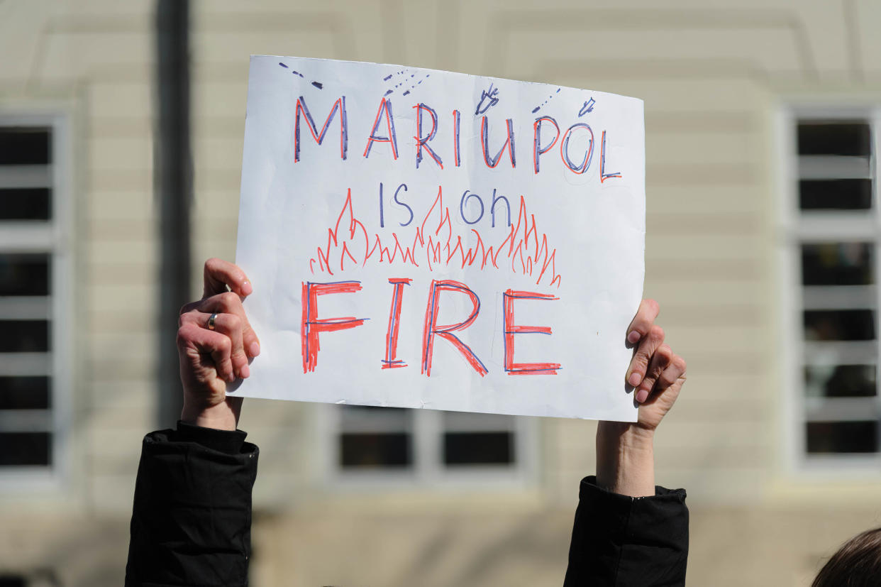 Protester holds a placard reading: Mariupol is on fire.