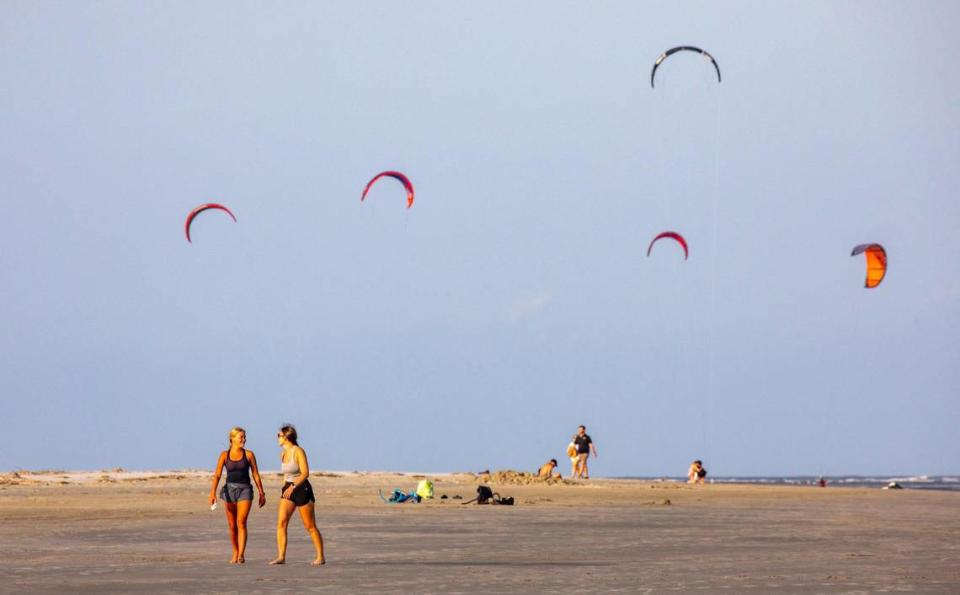Beachgoers walk the broad expanse of the Sullivan’s Island beach front as kiteboarder’s sails fly in the distance.