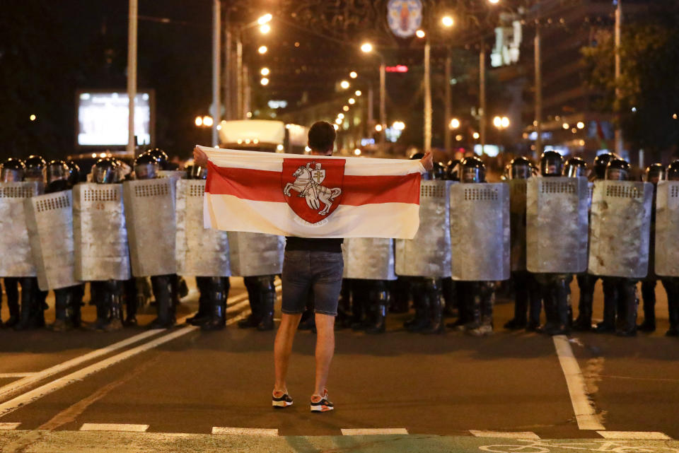 FILE - In this file photo taken on Sunday, Aug. 9, 2020, a protester holds an old Belarusian national flag as he stands in front of police during a demonstration against the disputed presidential election in Minsk, Belarus. Hundreds of people released from custody after a violent crackdown on protests in Belarus are sharing their accounts of harsh treatment at the hands of police. (AP Photo/Sergei Grits, File)