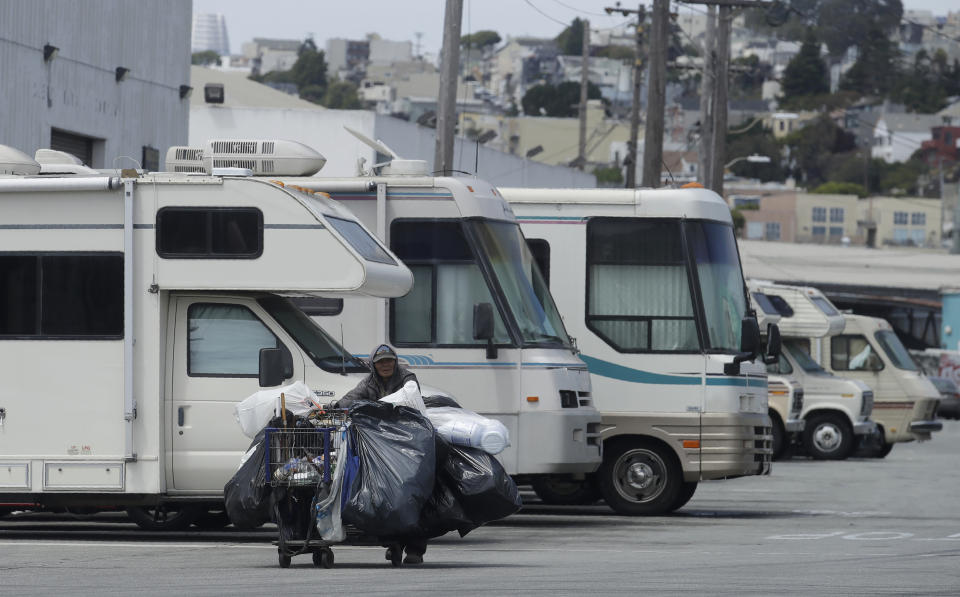 This Thursday, June 27, 2019, photo shows a person pushing a cart past parked RVs along a street in San Francisco. A federally mandated count of homeless in San Francisco increased 17% in two years, driven in part by a surge of people living in RVs and other vehicles. (AP Photo/Jeff Chiu)