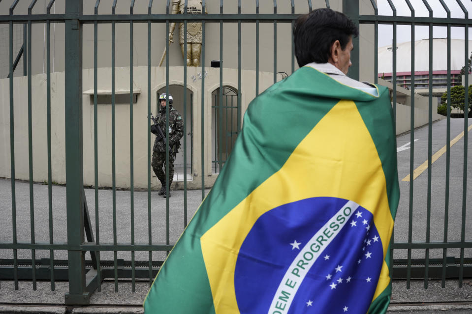 A supporter of Brazilian President Jair Bolsonaro stands wrapped in the national flag outside a military base during a protest against his reelection defeat in Sao Paulo, Brazil, Thursday, Nov. 3, 2022. Some supporters are calling on the military to keep Bolsonaro in power, even as his administration signaled a willingness to hand over the reins to his rival, President-elect Luiz Inacio Lula da Silva. (AP Photo/Matias Delacroix)