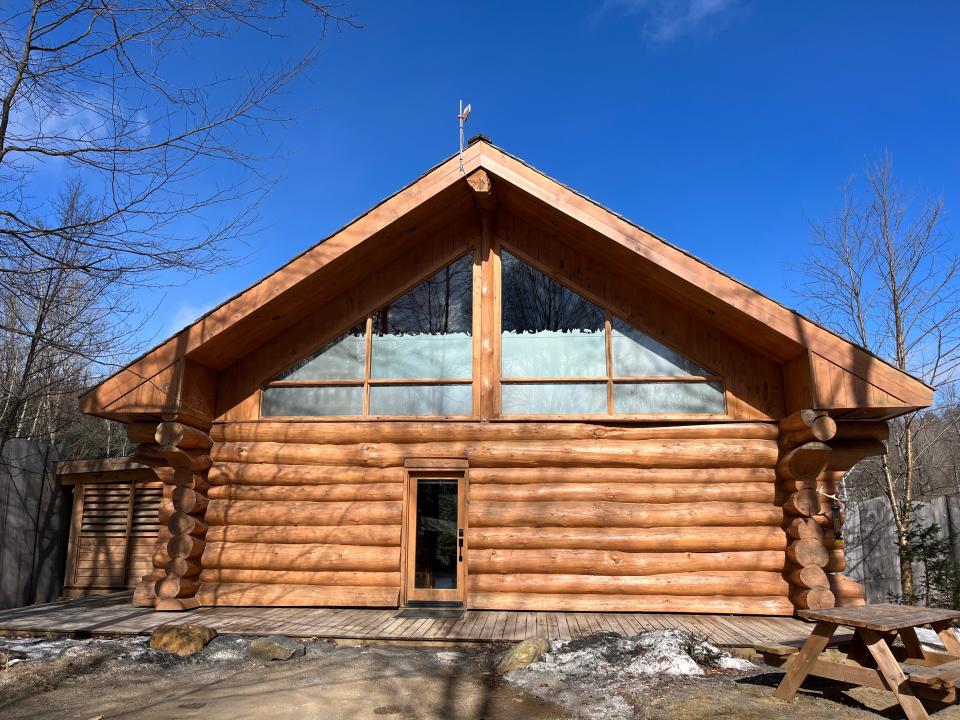 A completely wooden lodge with visible logs and a peaked roof in the wilderness with a bright-blue sky in the background