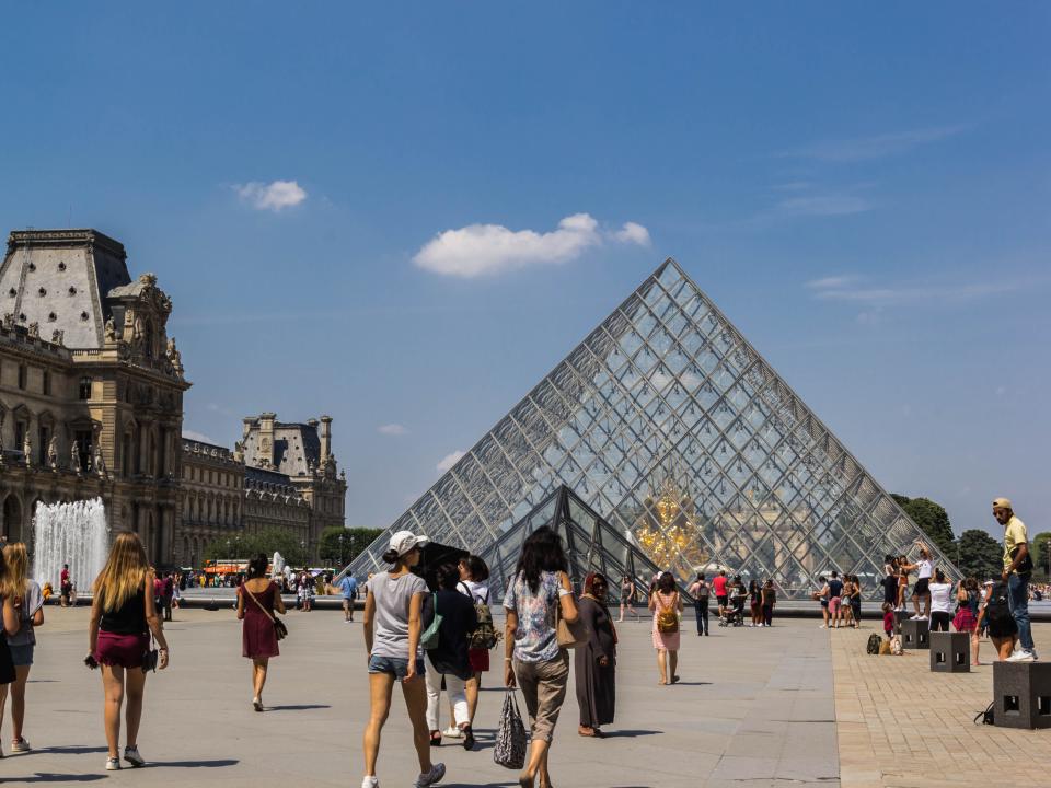people walking toward the pyramid entrance to the lourve museum in paris france