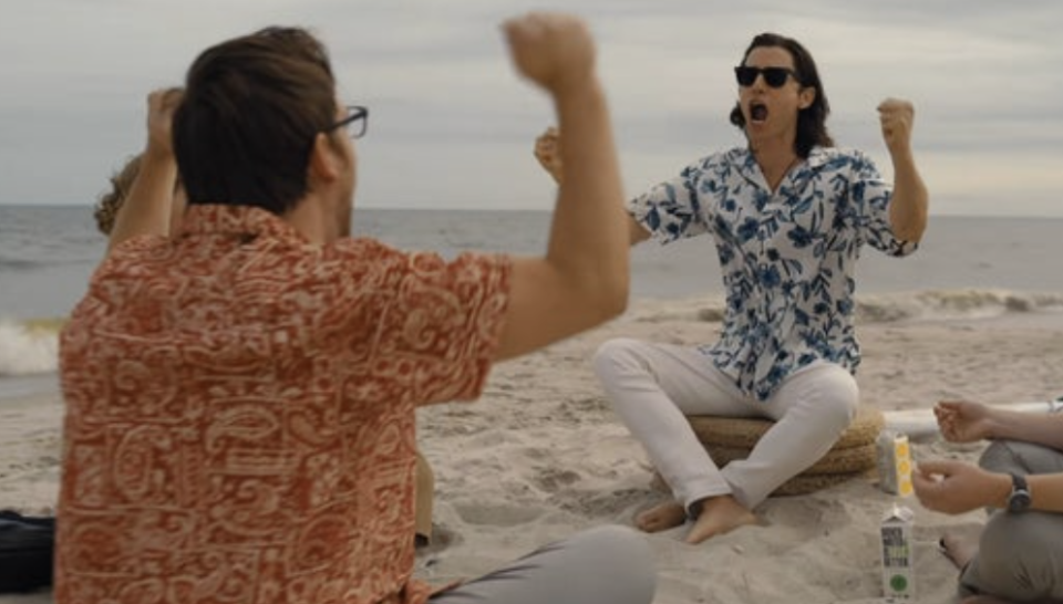 Jared Leto yells happily, sitting in a circle with his friends at a sea beach