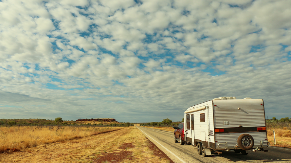 A caravan driving along an Australian road with a big blue clouded sky.