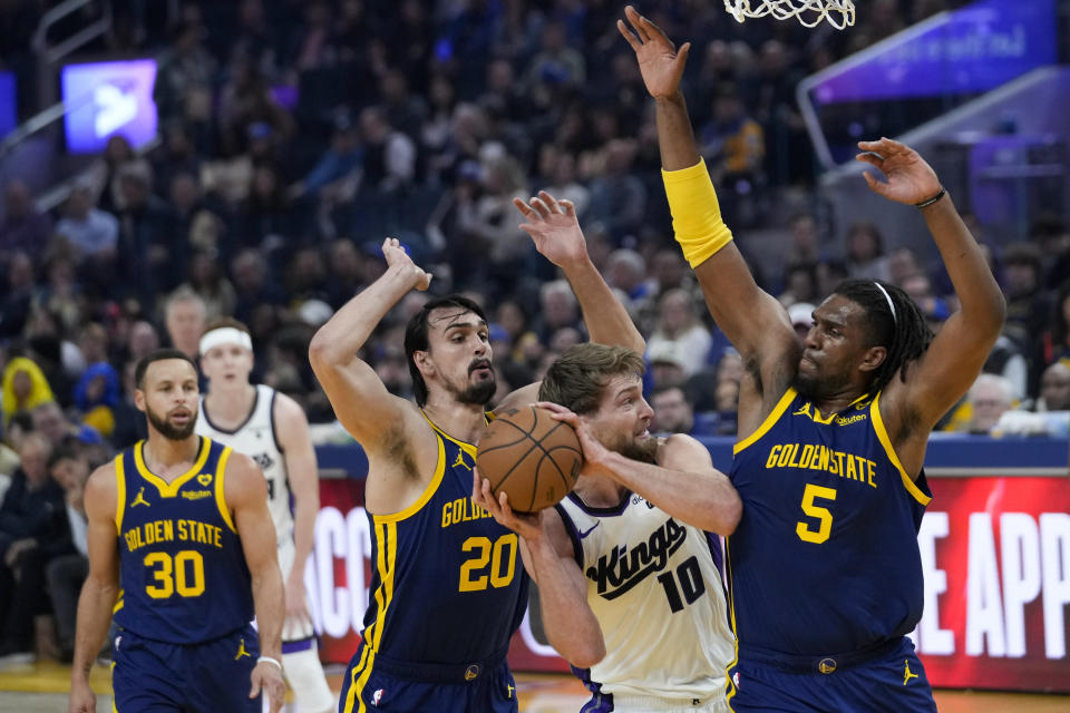 Sacramento Kings center Domantas Sabonis (10) tries to move between Golden State Warriors forward Dario Saric (20) and center Kevon Looney (5) during the first half of an NBA basketball game Thursday, Jan. 25, 2024, in San Francisco. (AP Photo/Godofredo A. Vásquez)