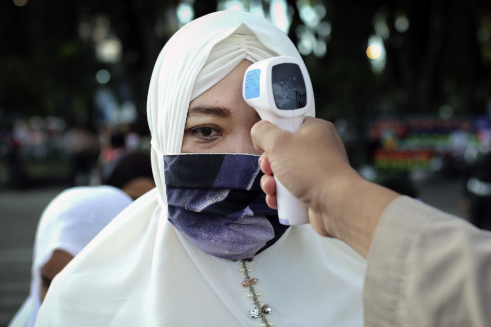 A security officer checks the temperature of a woman before she enters Baiturrahman Grand Mosque to attend an Eid al Fitr prayer in Banda Aceh in the deeply conservative Aceh province, Indonesia, Sunday, May 24, 2020. Millions of people in the world's largest Muslim nation are marking a muted and gloomy religious festival of Eid al-Fitr, the end of the fasting month of Ramadan - a usually joyous three-day celebration that has been significantly toned down as coronavirus cases soar. (AP Photo/Heri Juanda)