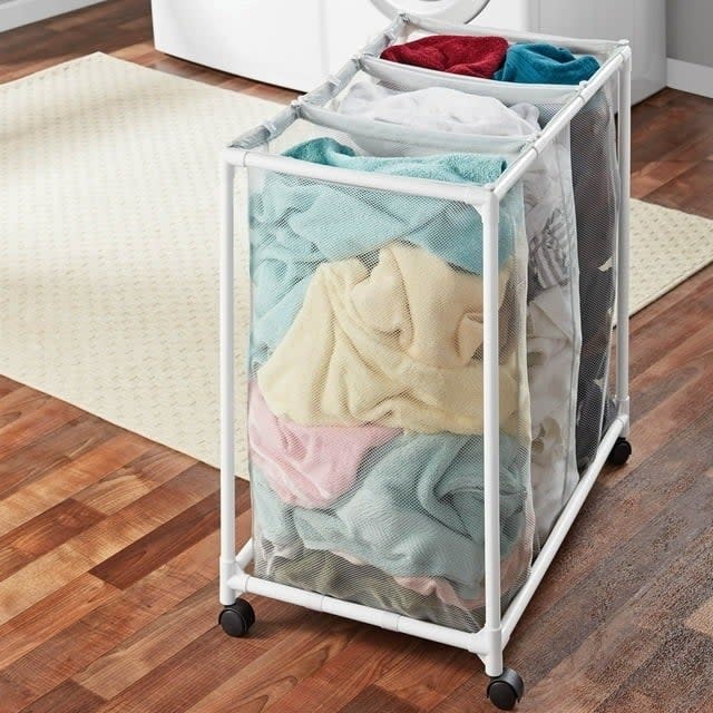 Mesh laundry sorter with wheels in a home setting, filled with assorted clothing