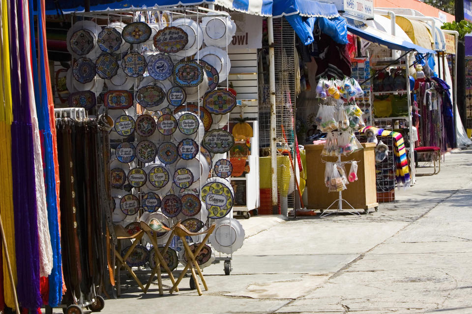 A bustling outdoor market street with shops selling colorful items, hand-painted ceramics, and textiles. Perfect for tourists exploring local crafts