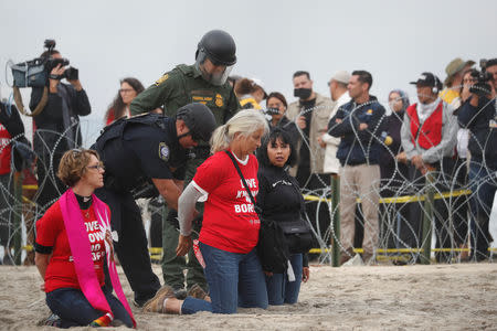 A police officer and a U.S. Customs and Border Protection (CBP) official detain women during a gathering in support of the migrant caravan in San Diego, U.S., close to the border wall between the United States and Mexico, as seen from Tijuana, Mexico December 10, 2018. REUTERS/Carlos Garcia Rawlins