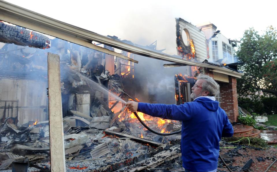 In this file photo, Oak Park resident Tom Duffy tries to put out flames in his neighbor's house after the Woolsey Fire swept the neighborhood.