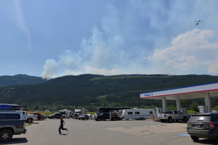 While a helicopter returns from surveying some of numerous wildfires in the area, people fill up gas and food at a service station on Little Fort, British Columbia, Canada July 9, 2017. REUTERS/Dennis Owen