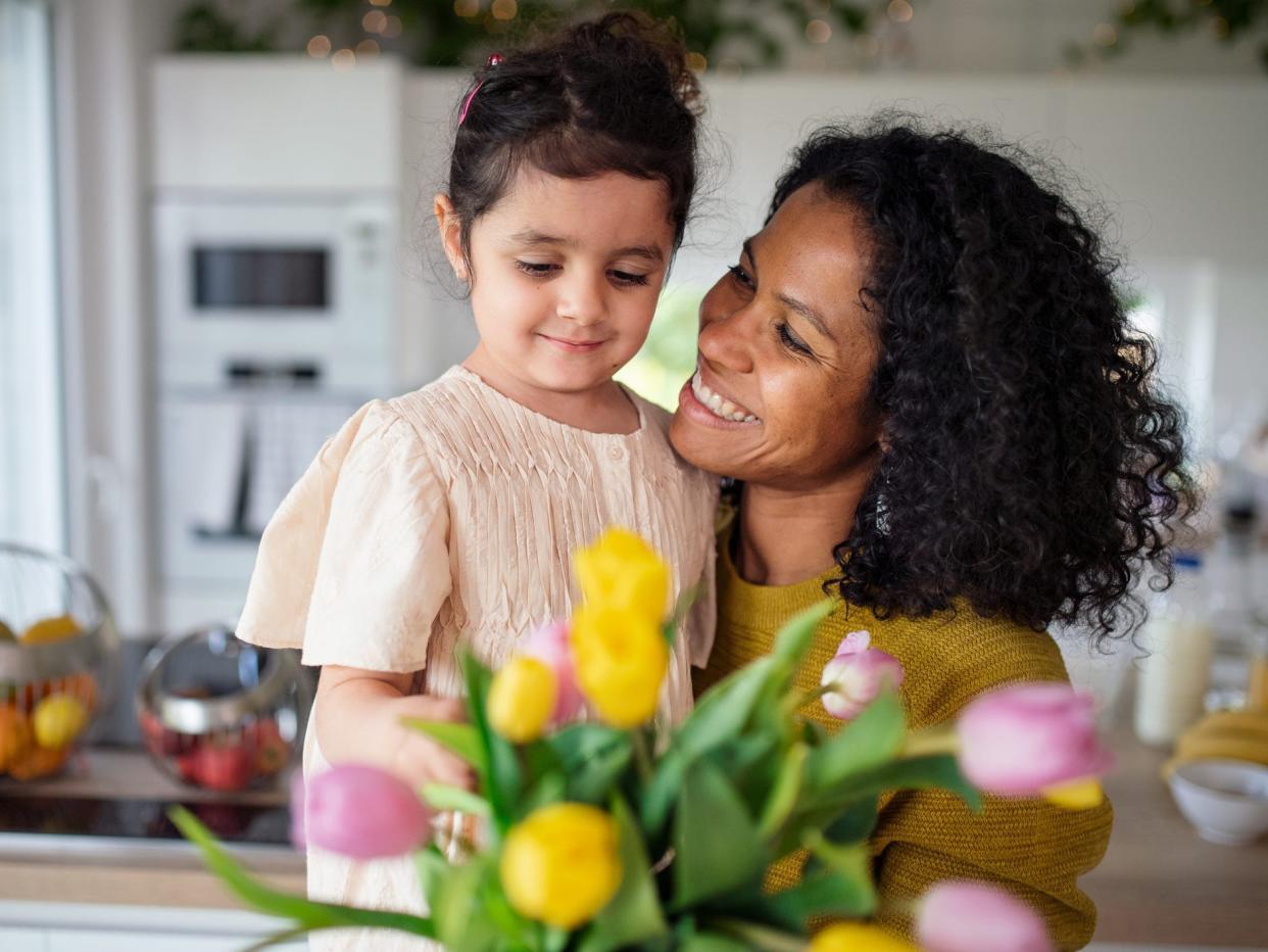 Multiracial girl giving flowers her mother in their kitchen, having fun