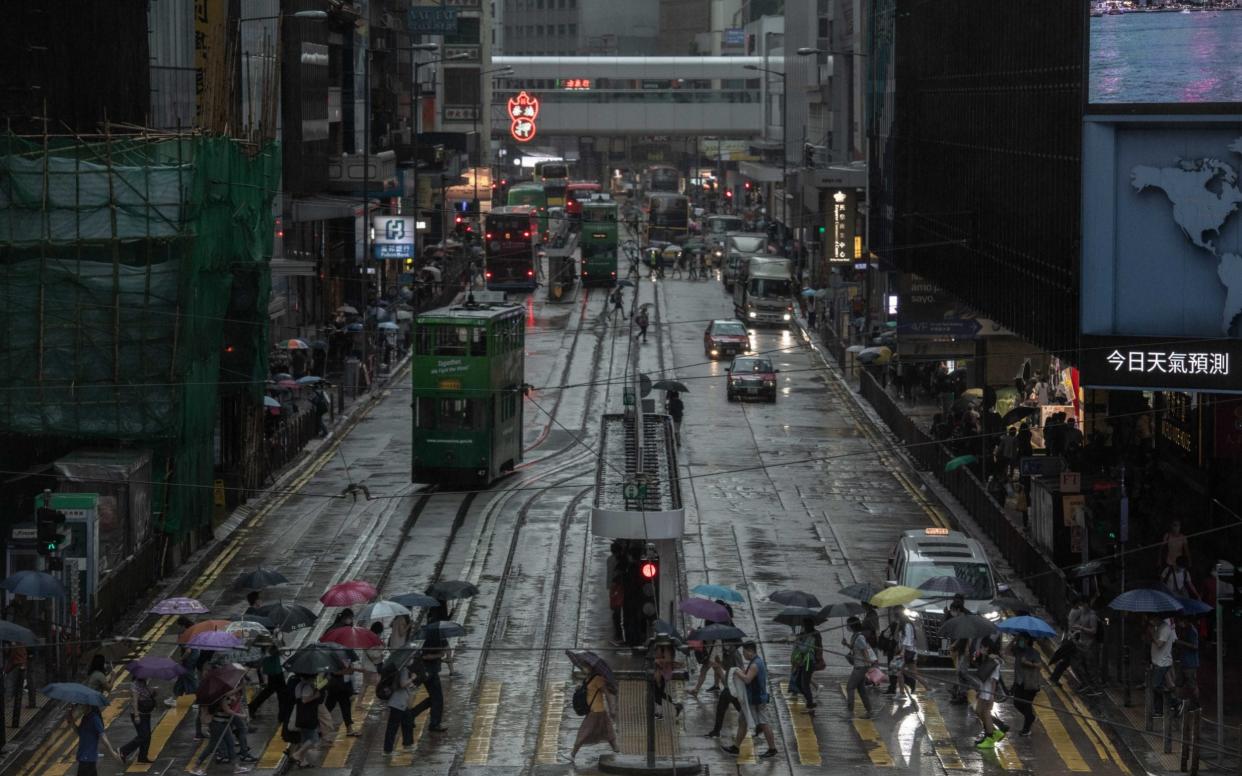 People holding umbrellas cross Des Voeux Road in the Central district in Hong Kong - Ivan Abreu/Bloomberg