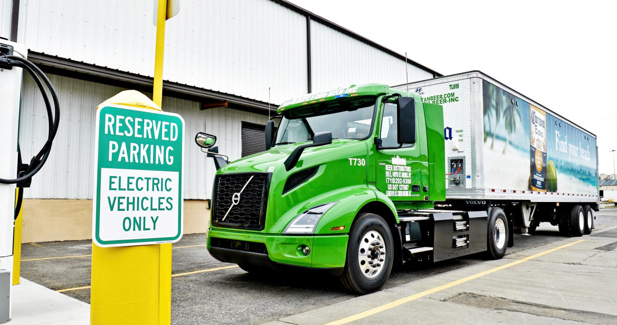 A green electric truck charges next to a sign that reads: Reserved Parking Electric Vehicles Only