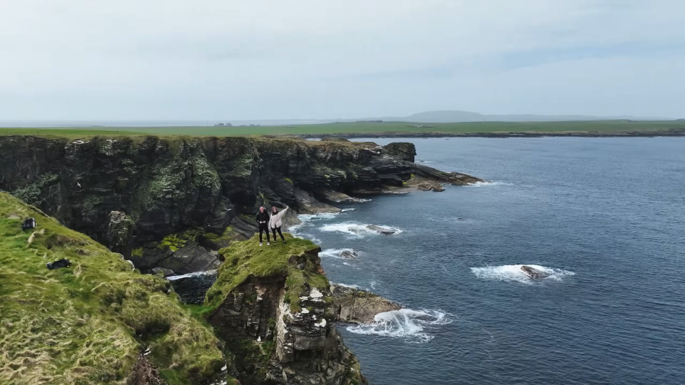 A man and woman standing along the rocky Scottish coastline