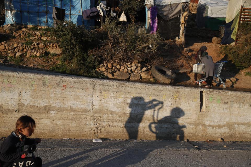 Children play as others put water on a shopping cart outside the perimeter of the overcrowded refugee camp at the port of Vathy on the eastern Aegean island of Samos, Greece, Tuesday, Feb. 23, 2021. On a hill above a small island village, the sparkling blue of the Aegean just visible through the pine trees, lies a boy’s grave. His first ever boat ride was to be his last - the sea claimed him before his sixth birthday. His 25-year-old father, like so many before him, had hoped for a better life in Europe, far from the violence of his native Afghanistan. But his dreams were dashed on the rocks of Samos, a picturesque Greek island almost touching the Turkish coast. Still devastated from losing his only child, the father has now found himself charged with a felony count of child endangerment. (AP Photo/Thanassis Stavrakis)