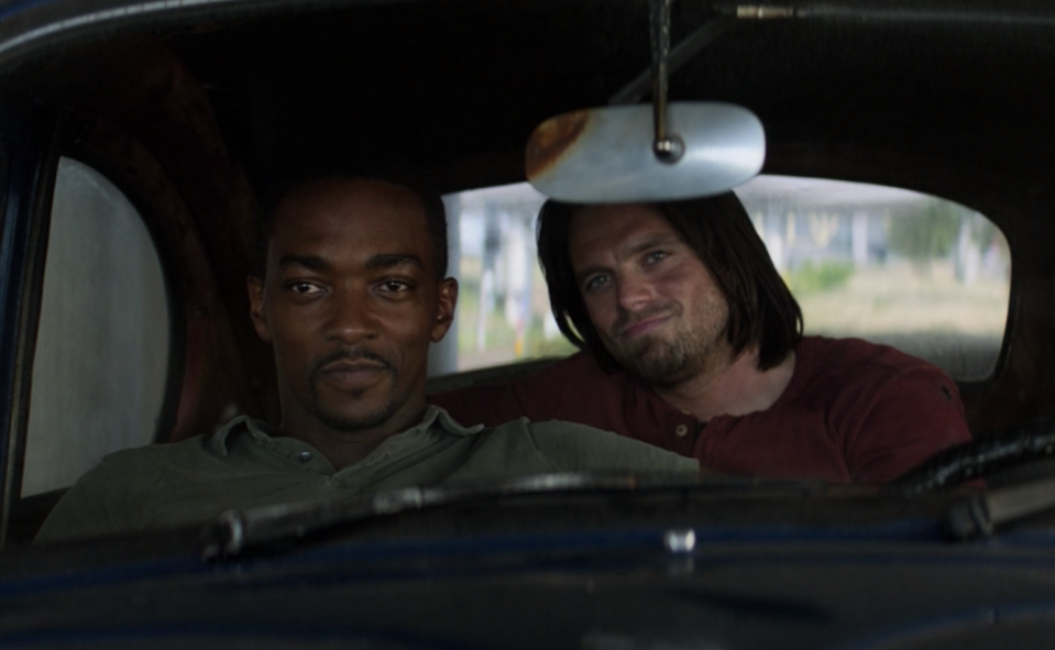 Sam Wilson smiles as he sits in the driver's seat of a car while Bucky Barnes sits behind him, smirking.