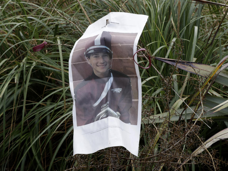 A photo from a student newspaper article from the Marjory Stoneman Douglas High School in Parkland, Florida, is attached to a tree planted at Halswell Quarry Park Conservation Area on the outskirts of Christchurch, New Zealand, Tuesday, July 24, 2018. The 28 students who survived the Feb. 14, 2018 mass-shooting at the Florida school are visiting New Zealand to learn how to sustain a youth movement. New Zealand's Student Volunteer Army, started after the deadly 2011 earthquake in Christchurch, is seen as a good example. (AP Photo/Mark Baker)