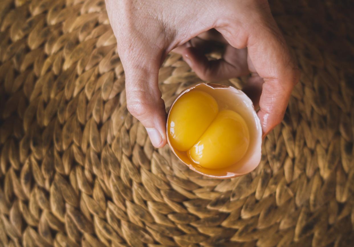 A person holding a raw egg with two yolks