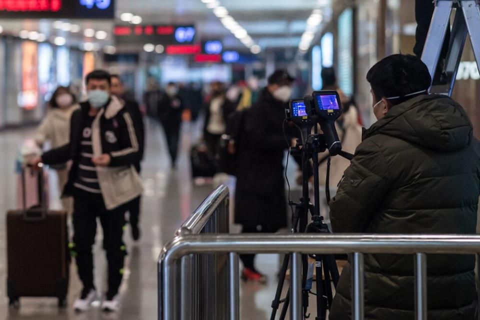 A worker operates two advanced thermo cameras to check the body temperature of travelers at the arrival area of Beijing West Railway Station in Beijing.  | NICOLAS ASFOURI/Getty Images