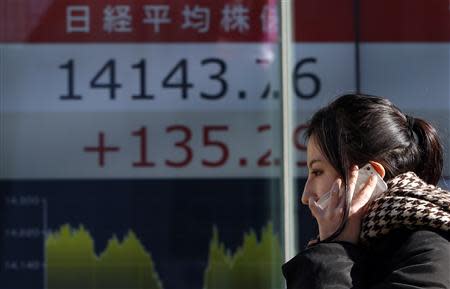 A pedestrian holding her mobile phone walks past an electronic board showing Japan's Nikkei average outside a brokerage in Tokyo February 5, 2014. REUTERS/Yuya Shino