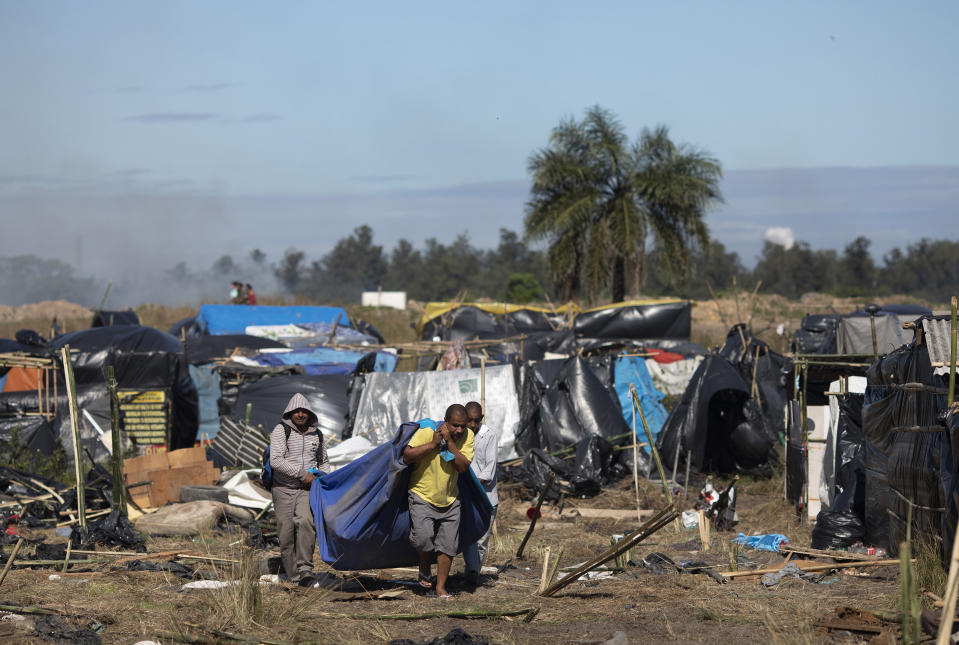 People carry their belongings after they were evicted from land designated for a Petrobras refinery, at a settlement coined the "First of May Refugee Camp," named for the date people moved in setting up tents and shacks, in Itaguai, Rio de Janeiro state, Brazil, Thursday, July 1, 2021, amid the new coronavirus pandemic. (AP Photo/Silvia Izquierdo)