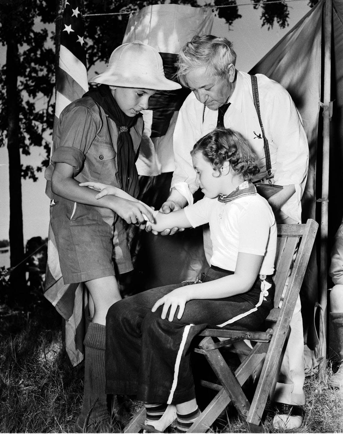 July 4, 1938: Catholics celebrate 4th of July with picnic at Lake Worth; Charles Edward Breen in Boy Scout uniform bandages a scratch on his sister’s arm (Patsy) while supervised by Dr. M.V. Creagan. Fort Worth Star-Telegram archive/UT Arlington Special Collections