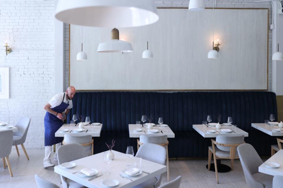 A waiter in a white dining room with dark blue banquette booths