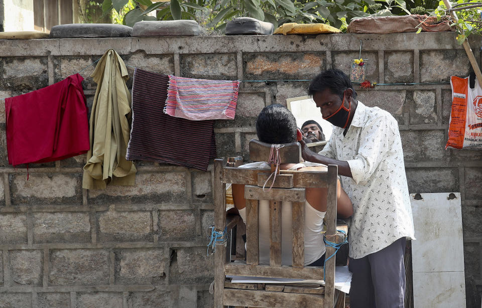 A roadside barber wearing face mask as a precaution against the coronavirus gives a shave in Hyderabad, India, Saturday, Jan. 2, 2021. (AP Photo/Mahesh Kumar A.)