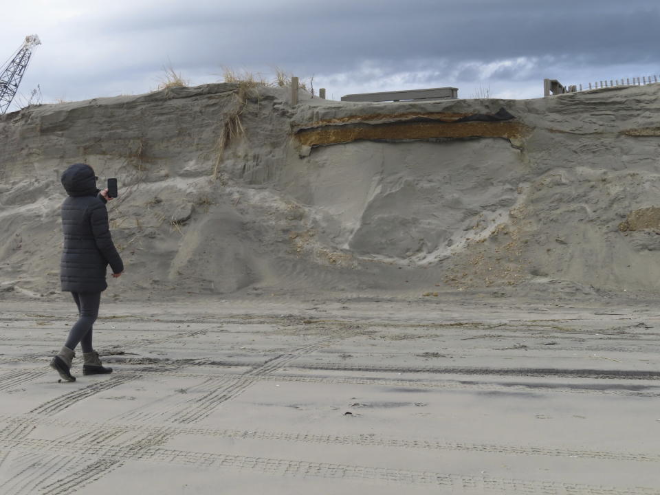 A beachgoer takes a photo of a severely eroded dune in North Wildwood, N.J. on Jan. 5, 2023 where a ramp down to the beach used to exist but now dead-ends in mid-air. North Wildwood, which is defying a state order not to do emergency repairs to its eroded beach, is suing New Jersey for $21 million, asserting it has spent that amount trucking sand in to widen its beaches in the absence of a government beach replenishment project. (AP Photo/Wayne Parry)