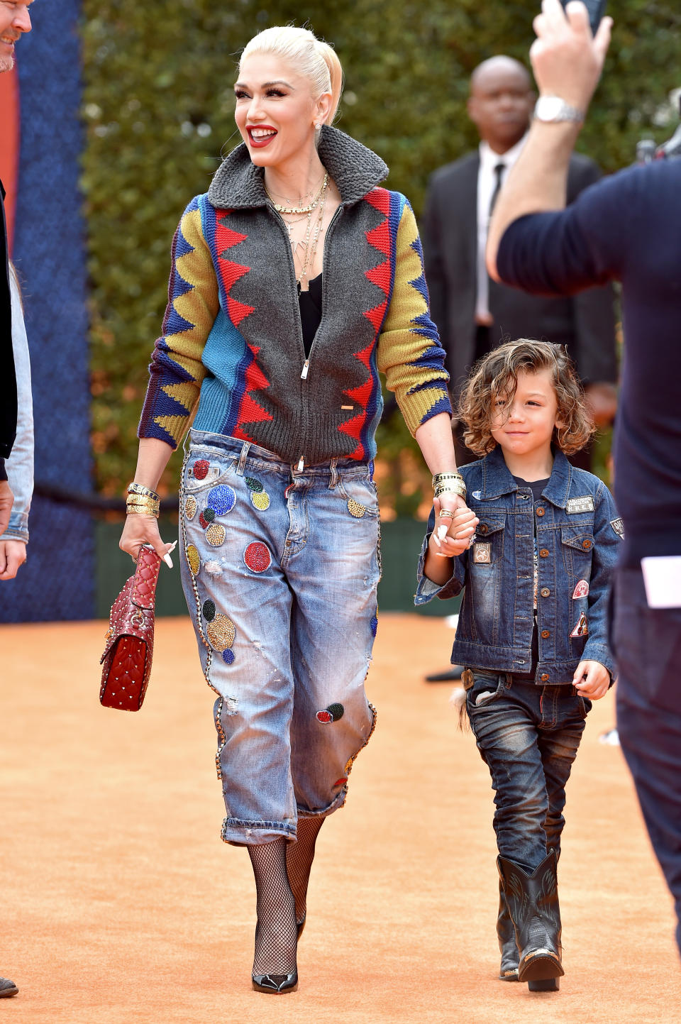 Gwen Stefani, wearing a patterned jacket and patched jeans, holding hands with her son, Apollo Bowie Flynn Rossdale, who is dressed in a denim jacket and jeans