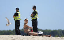 A woman sunbathes, while police patrol nearby, as a meeting of G7 leaders takes place in St. Ives, Cornwall, England, Saturday, June 12, 2021. Leaders of the G7 gather for a second day of meetings on Saturday, in which they will discuss COVID-19, climate, foreign policy and the economy. (AP Photo/Jon Super)