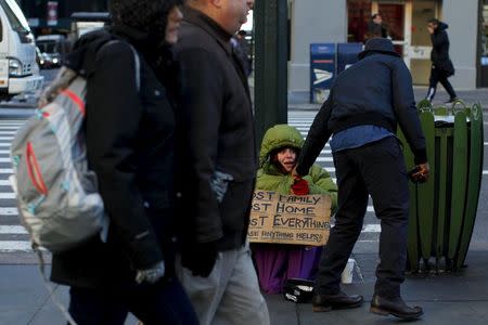 A homeless woman sits bundled against the cold as she receives a handout from a passerby on East 42nd Street in the Manhattan borough of New York City, January 4, 2016. REUTERS/Mike Segar