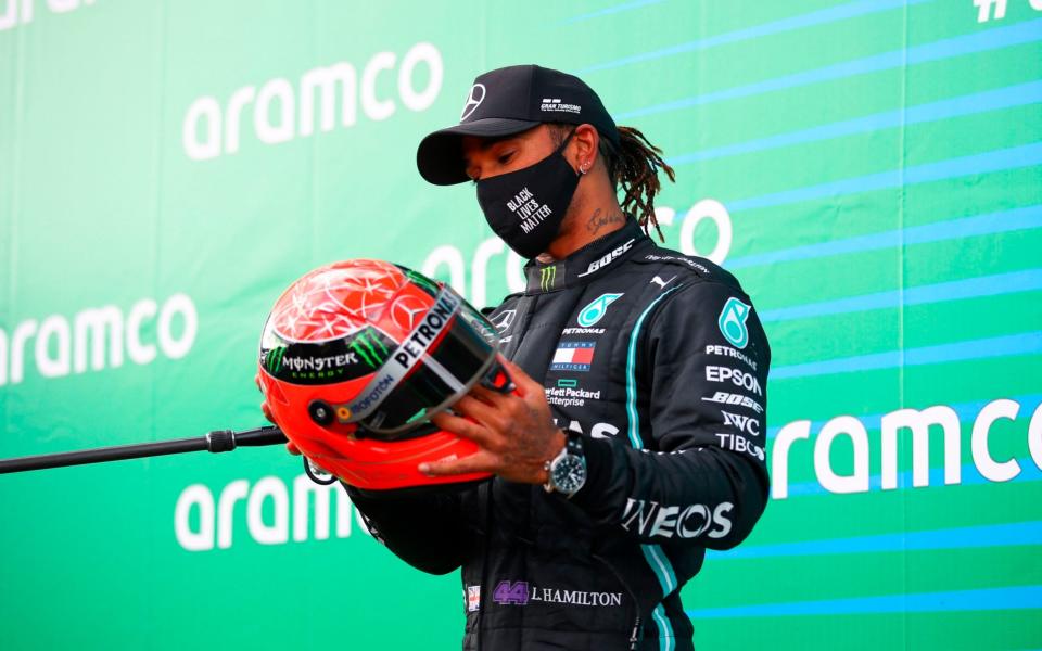 Winner Mercedes' British driver Lewis Hamilton holds the red helmet of former German Formula one champion Michael Schumacher that was offered to him by Mick Schumacher (unseen) on the podium after the German Formula One Eifel Grand Prix at the Nuerburgring circuit in Nuerburg, western Germany, on October 11, 2020. - Lewis Hamilton equalled Michael Schumacher's record of 91 Formula One wins on on October 11, 2020 when he guided his Mercedes to a narrow, if measured, victory at Eifel Grand Prix. Schumacher's 21-year-old son Mick, a rising star and leader of the F2 series, presented Hamilton with a red helmet from his father's career collection - AFP/BRYN LENNON 