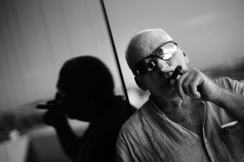 This Feb. 27, 2017 photo shows Associated Press photojournalist Desmond Boylan smoking a cigar on the balcony of the agency's office in Havana, Cuba. Boylan, a photographer who covered war and conflict across the world before dedicating his life to documenting the joys and tribulations of daily life in Cuba for The Associated Press, died suddenly on Saturday afternoon, Dec. 29, 2018, in Havana. He was 54. (AP Photo/Ramon Espinosa)