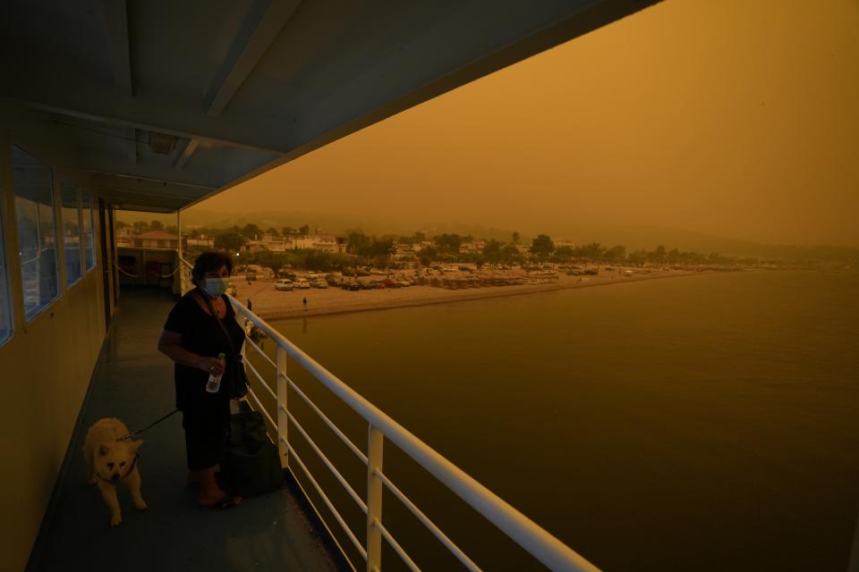 People use a ferry to evacuate from Pefki village on Evia island, about 189 kilometers (118 miles) north of Athens, Greece, Sunday, Aug. 8, 2021. Pillars of billowing smoke and ash are blocking out the sun above Greece's second-largest island as a days-old wildfire devours pristine forests and triggers more evacuation alerts. (AP Photo/Petros Karadjias)