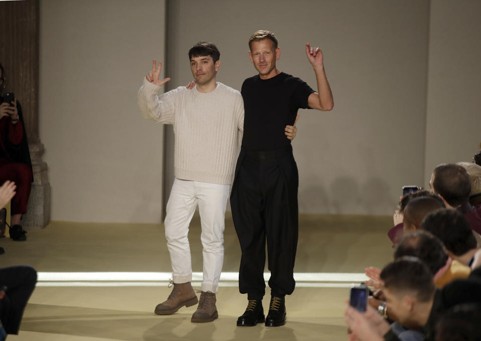 Creative director Paul Andrew, right, accept applause flanked by menswear designer Guillaume Meilland, at the conclusion of the the Salvatore Ferragamo men's Fall-Winter 2020/21 fashion show, that was presented during the fashion week, in Milan, Italy, Sunday, Jan. 12, 2020. (AP Photo/Luca Bruno)