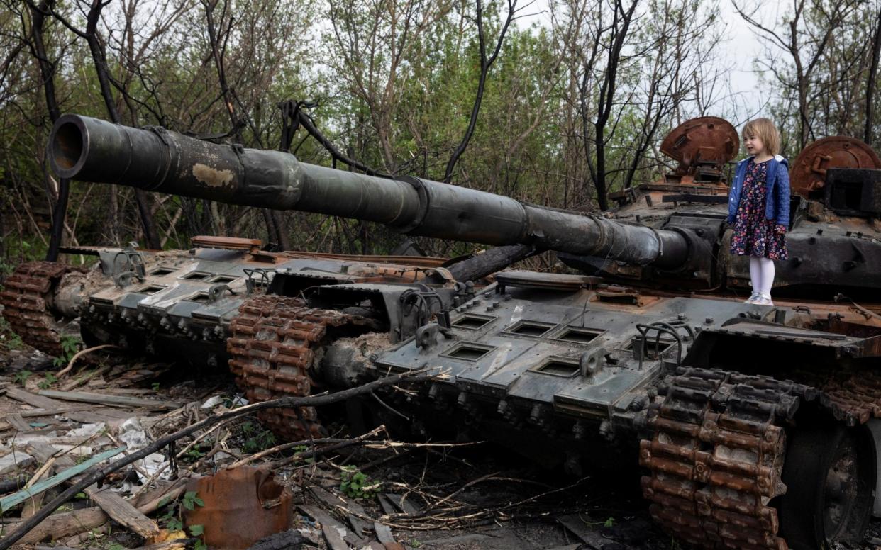 A child stands on a destroyed Russian tank near Makariv, Kyiv region, Ukraine - Mikhail Palinchak/Reuters