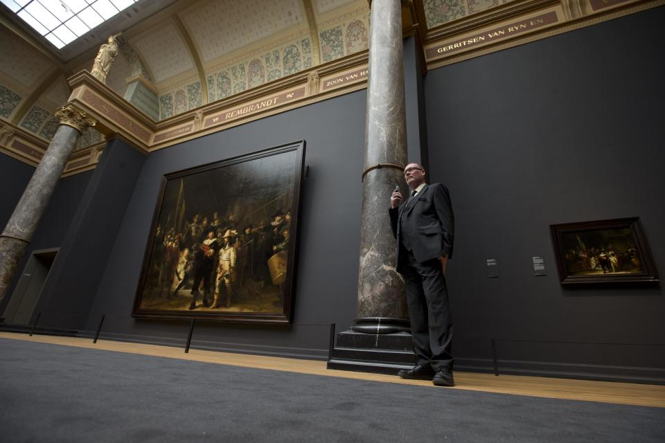 A senior security officer stands next to Dutch master Rembrandt's The Night Watch painting, left, and a copy of The Night Watch by Gerrit Lundens, right, during a press preview of the renovated Rijkmuseum in Amsterdam, Thursday, April 4, 2013. The Rijksmusuem, home of Rembrandt's Night Watch and other national treasures, is preparing to reopen its doors on April 13, 2013 after a decade-long renovation. (AP Photo/Peter Dejong)