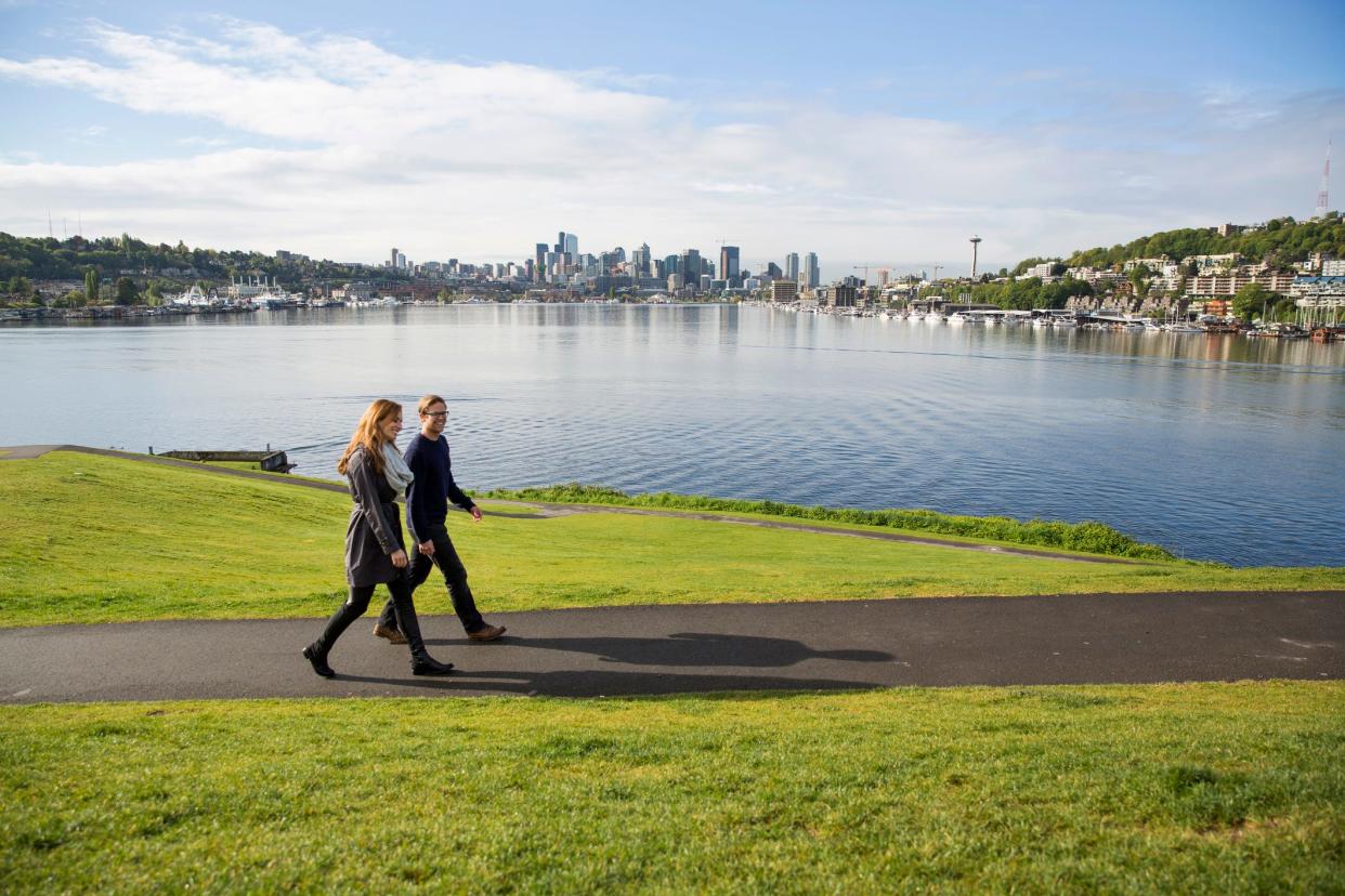 a pair of people walking on the waterfront with a city in the background